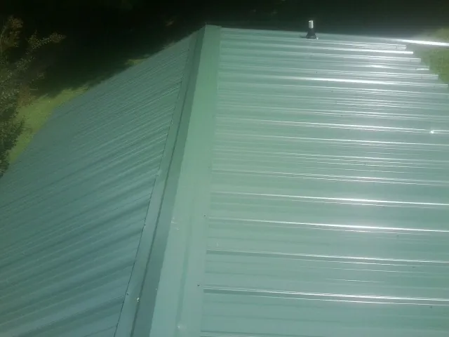 New green metal panels meeting at the ridge of a roof — Flat Roof Repair work by our crew in Lake Mills