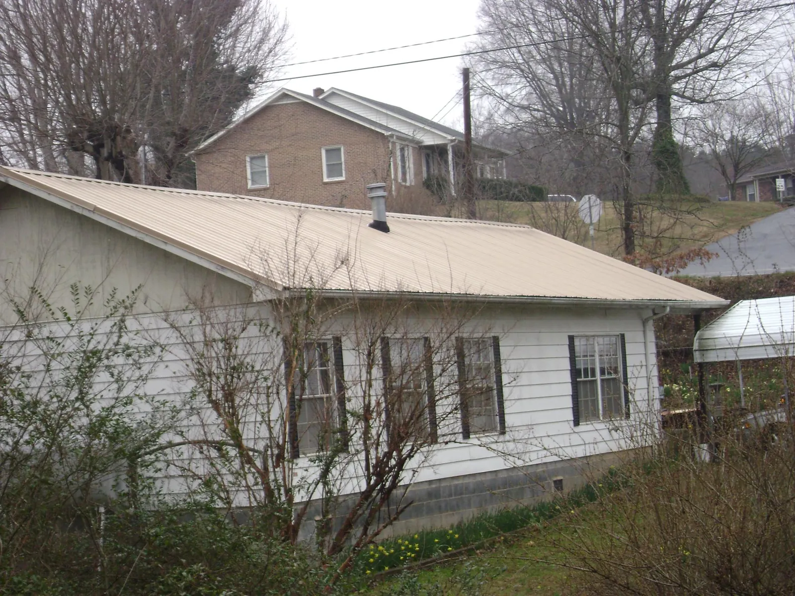 Tan metal roof on a white sided house set into a hillside — Commercial Roofing by Roofing Brothers in Lake Mills