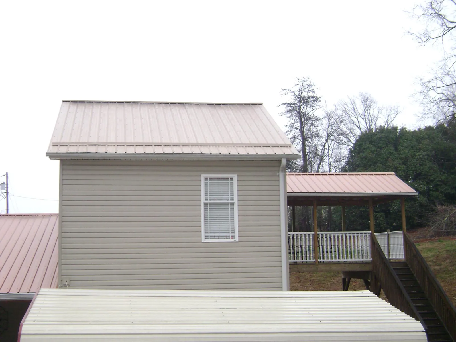 Tan metal roofs on a two story addition and attached porch, from a Roof Replacement job in Lake Mills